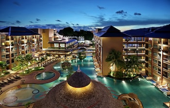Relax by the pool with lounge chairs and umbrellas, surrounded by lush landscaping and a central water feature.