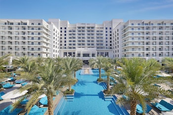 Um resort com uma grande piscina, palmeiras e vista para o horizonte da cidade.