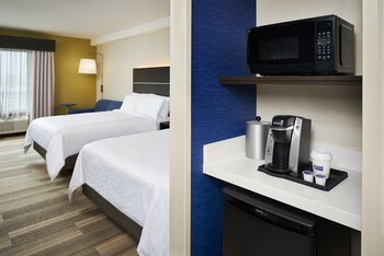 Quarto de hotel com uma cama grande, uma escrivaninha com televisão de tela plana, uma cadeira, uma mesa pequena e uma janela com cortinas.