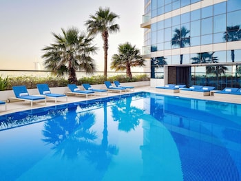 A rooftop pool area with lounge chairs, palm trees, and a view of the cityscape.