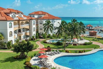 Piscina de resort con vista al atardecer, palmeras y un edificio con balcones.