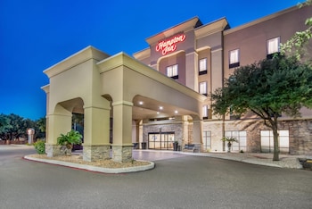 Un Hampton Inn con entrada cubierta, fachada de piedra y cielo azul despejado.