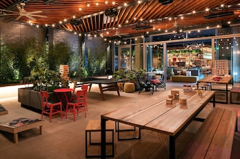 A modern lounge area with a long wooden table, red chairs, and a brick wall.