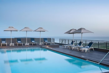A rooftop pool area with lounge chairs, umbrellas, and a bar.