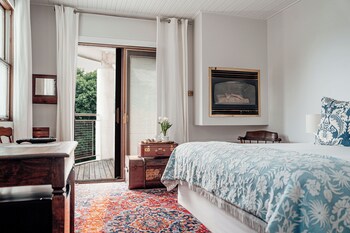 A room with a window, a wooden table, a vase with flowers, a cup, and a plate with pastries.