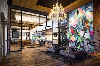 A modern hotel bar with a large mural, a chandelier, and a seating area with sofas and tables.