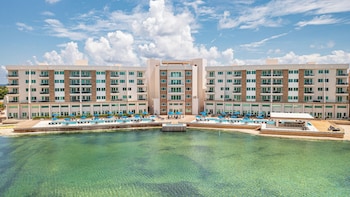 An underwater view of a swimming pool with a person swimming, clear blue water, and several blue umbrellas in the background.