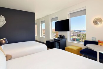 A hotel room with a large bed, a small table, a sofa, a TV, and a window with a city view.