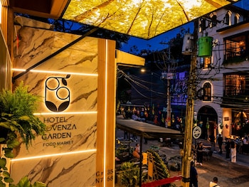 Un área de estar al aire libre con plantas en macetas y mesas, un cartel de hotel y un mercado al fondo.