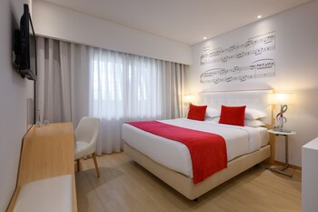 A modern hotel lobby with a central staircase, illuminated wall sconces, and large windows offering views of the city.