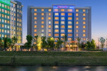 A multi-story hotel with a prominent 'Hampton Inn' sign, surrounded by greenery and a body of water.