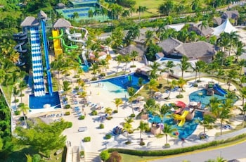 A resort with a large pool, water slides, palm trees, and thatched-roof structures.