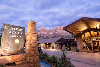 Un alojamiento con un cartel que dice "Cliffrose Lodge & Gardens", fachada de piedra y montañas al fondo.