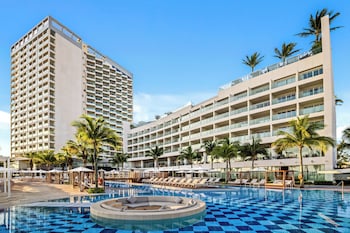Un hotel con piscina en la azotea, vista al mar y un edificio grande con balcones.