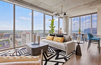Un salon moderne doté d’une grande fenêtre, d’un canapé, d’une table basse et d’un coin repas avec des chaises.