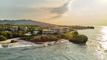 An aerial view of a resort with multiple buildings, a central pool area, and a beachfront.