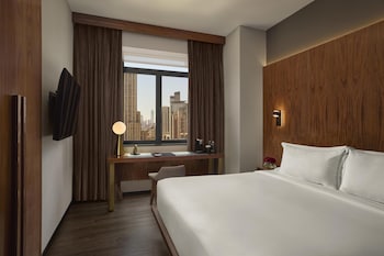 A hotel room with a wooden wardrobe, a white robe hanging on the door, and a bed with white bedding.