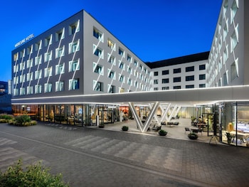 A modern hotel with a geometric facade, multiple balconies, and outdoor seating areas.