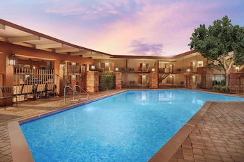 Un hotel con piscina, mobiliario exterior y montañas al fondo.