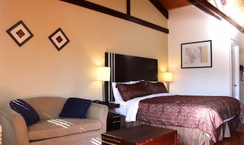 A hotel room with a bed, a nightstand, a lamp, a sofa, and two framed pictures on the wall.