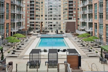 A rooftop pool area with lounge chairs and a smaller pool, surrounded by high-rise residential buildings.