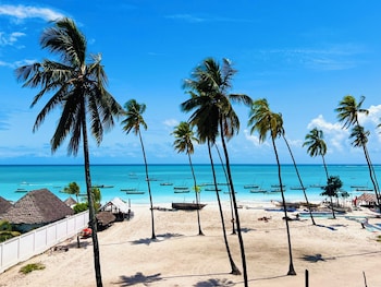 A beach with palm trees, clear blue water, and boats.
