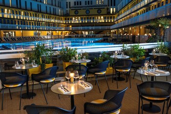 A large indoor swimming pool with a glass ceiling, multiple levels of balconies, and lounge areas with sun loungers.
