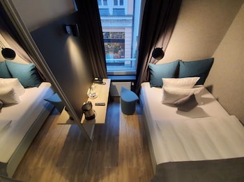 A modern hotel room with two beds, a small table, and a view of the street outside.