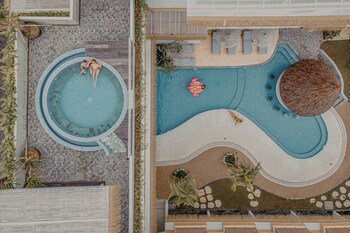 Un balcón con techo de paja, una piscina y una cama con cojín estampado.