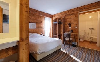 A cozy log cabin interior with a leather sofa, a vintage blue chair, a wooden cabinet, and a television on the wall.
