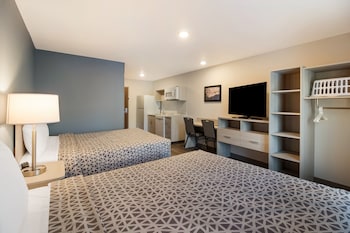 Een hotel met meerdere verdiepingen en een modern design, met een opvallende entree met overdekt gedeelte en een parkeerplaats met een rode SUV.