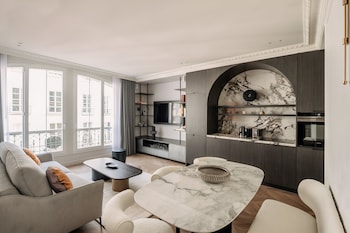 Una sala de estar moderna con una mesa de mármol, sofá y una cocina con horno empotrado y televisor.