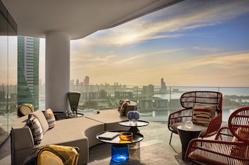 A modern hotel with a rooftop pool, a view of the cityscape, and a distinctive building with blue lights in the background.