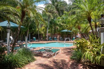 A pool area with lounge chairs, palm trees, and a building with balconies.