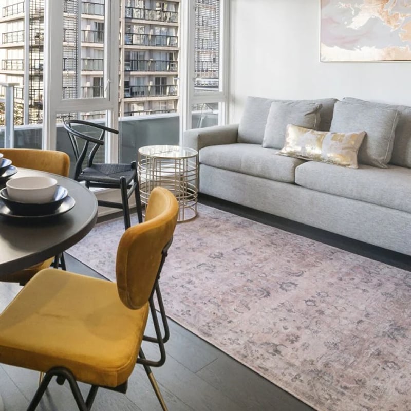 Un espace de vie ouvert dans un appartement, avec une table à manger et quatre chaises jaune moutarde, un canapé gris et un balcon avec vue sur les gratte-ciel de l’Ontario. 