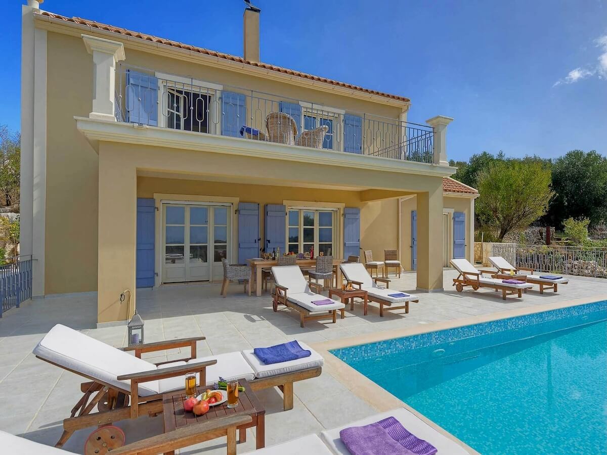 Une maison bordée d’arbres avec terrasses aux deux étages, l’une munie d’une piscine, de transats et d’un coin repas.