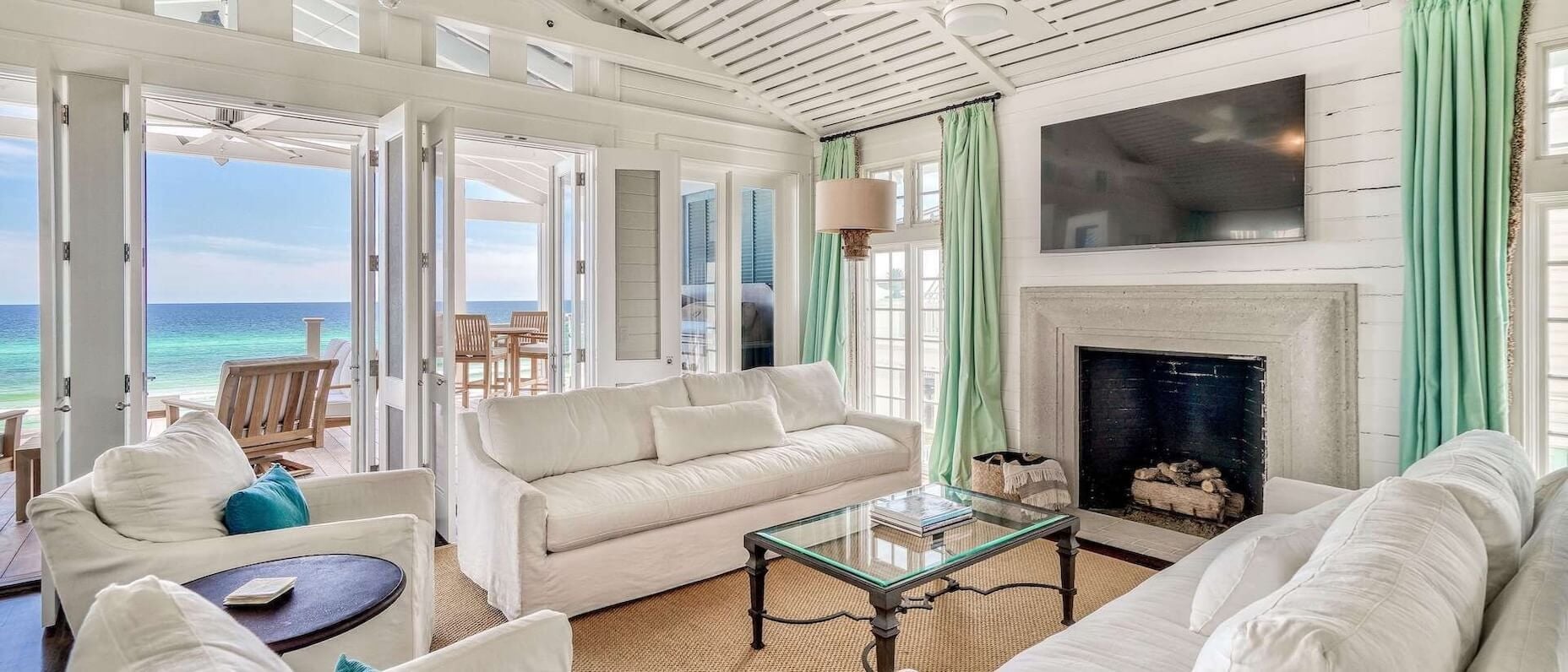 An indoor living space in a beachfront property with sofas, a coffee table and a fireplace. There is outdoor seating with a view of the sea.
