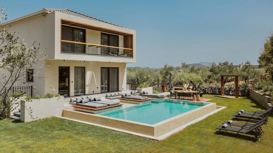 Une maison à deux étages avec piscine privée. Dans le jardin verdoyant se trouvent des lits bain de soleil et un coin repas.