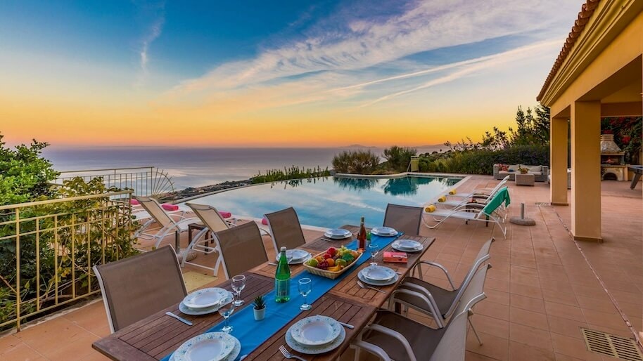 A private infinity pool at sunset, surrounded by sun loungers and a dining table with place settings and a bowl of fruit.