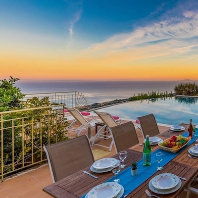 A private infinity pool at sunset, surrounded by sun loungers and a dining table with place settings and a bowl of fruit.
