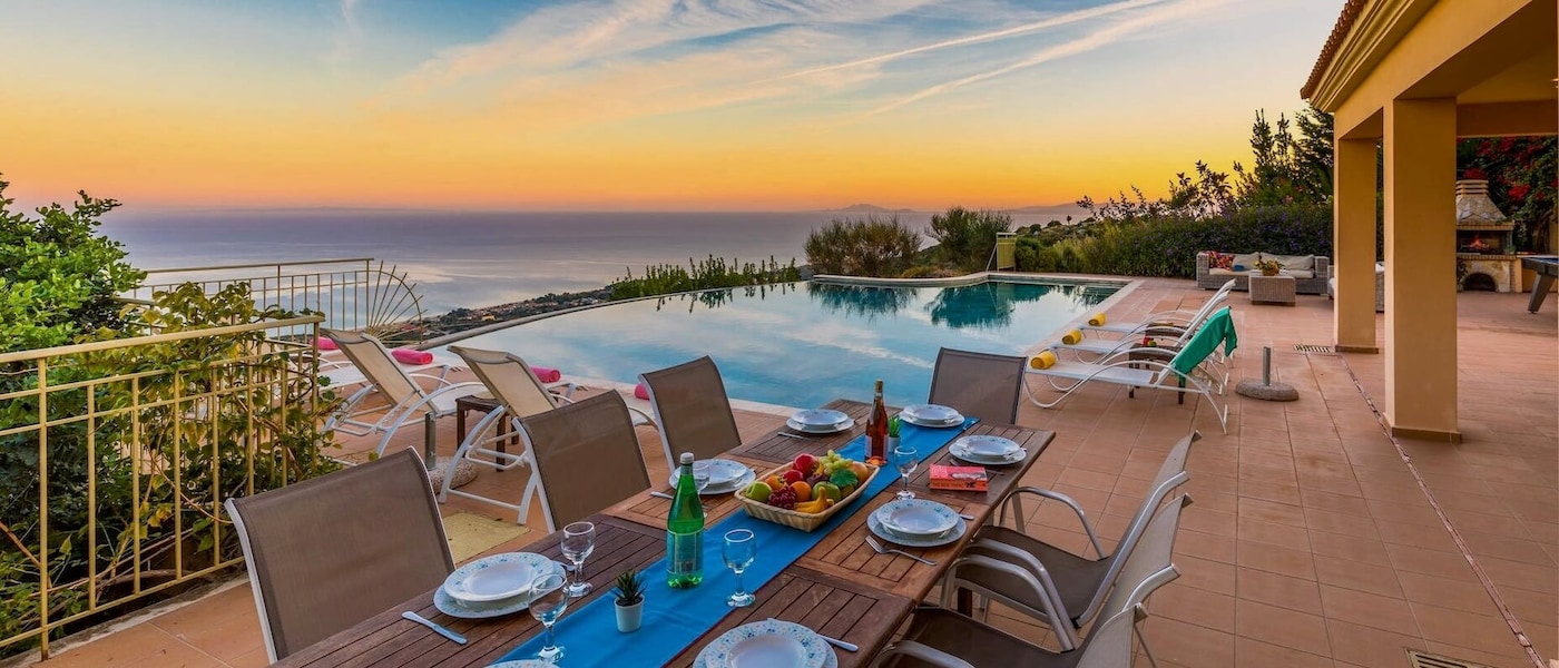 A private infinity pool at sunset, surrounded by sun loungers and a dining table with place settings and a bowl of fruit.