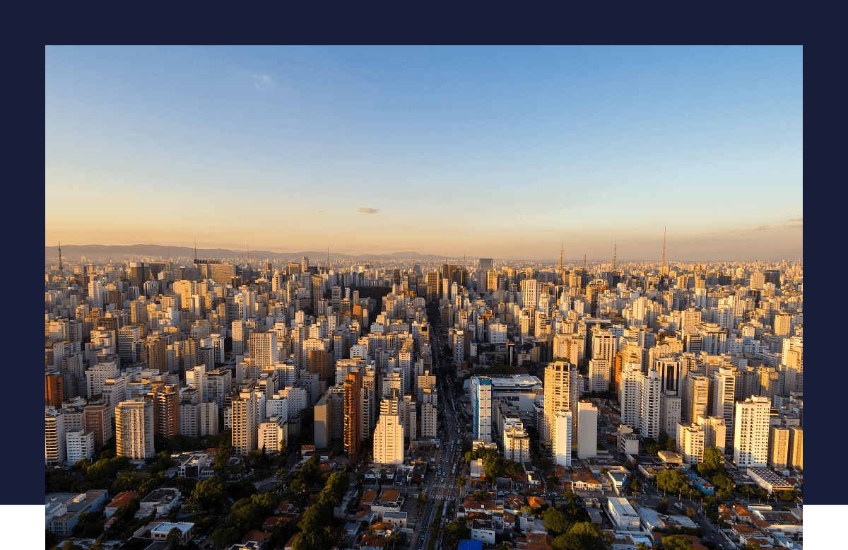 Vue panoramique d’une ville avec des gratte-ciel en bord de mer, végétation luxuriante au premier plan et océan en fond.