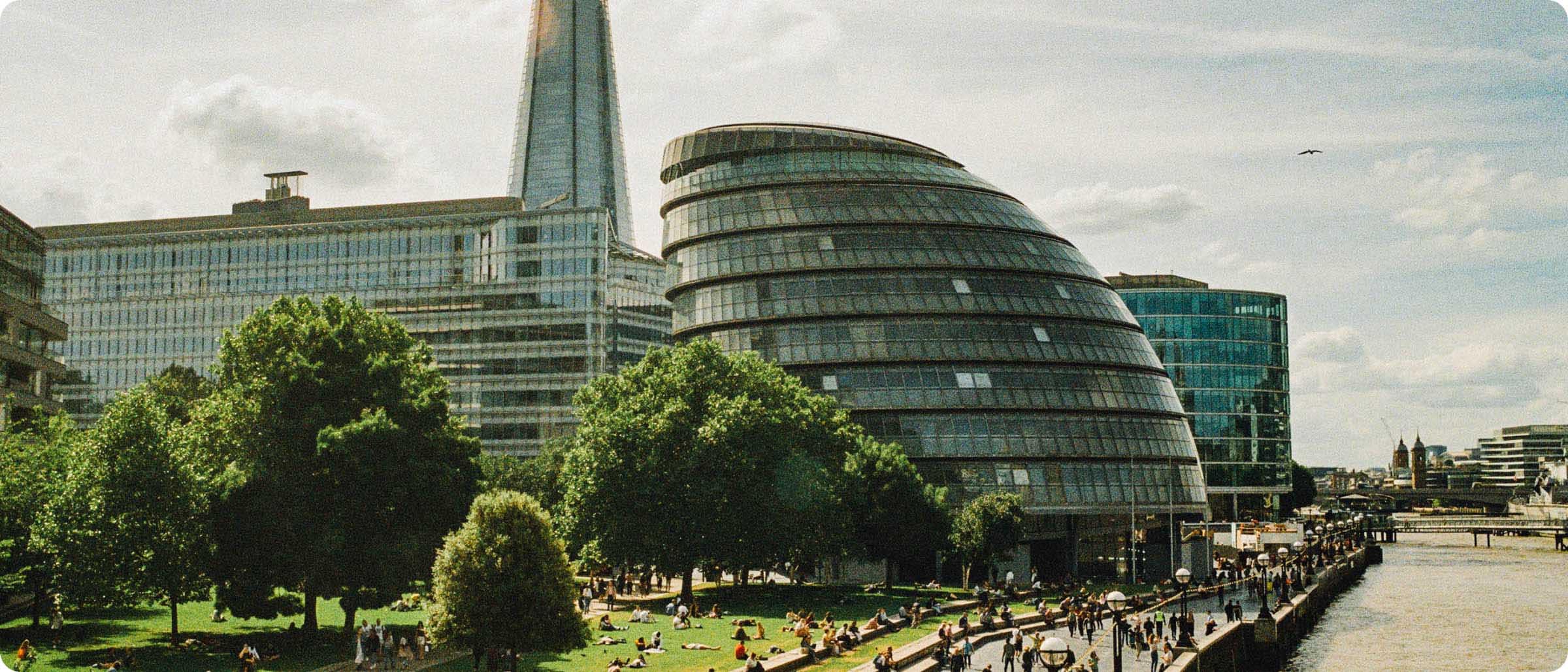 Einige Personen spazieren entlang der Themse, zu sehen sind Exemplare moderner Architektur in London, darunter The Shard und die City Hall.