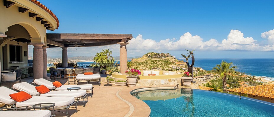 Person swimming laps in a long outdoor pool at a modern home, with sun loungers and palm trees in the background.