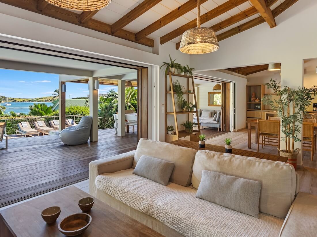Une villa ensoleillée au décor naturel, qui donne sur une terrasse bordée de chaises longues en bord de plan d’eau.