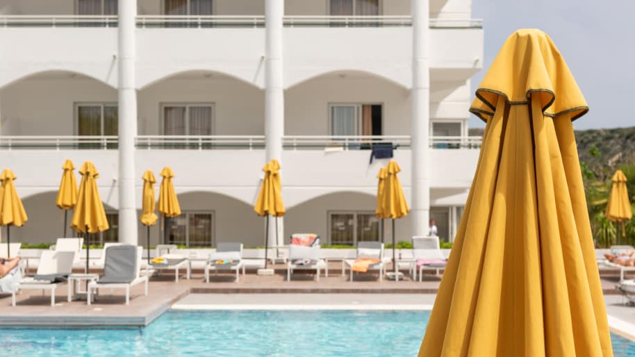 A sunny hotel resort with yellow umbrellas and lounge chairs around a turquoise pool.