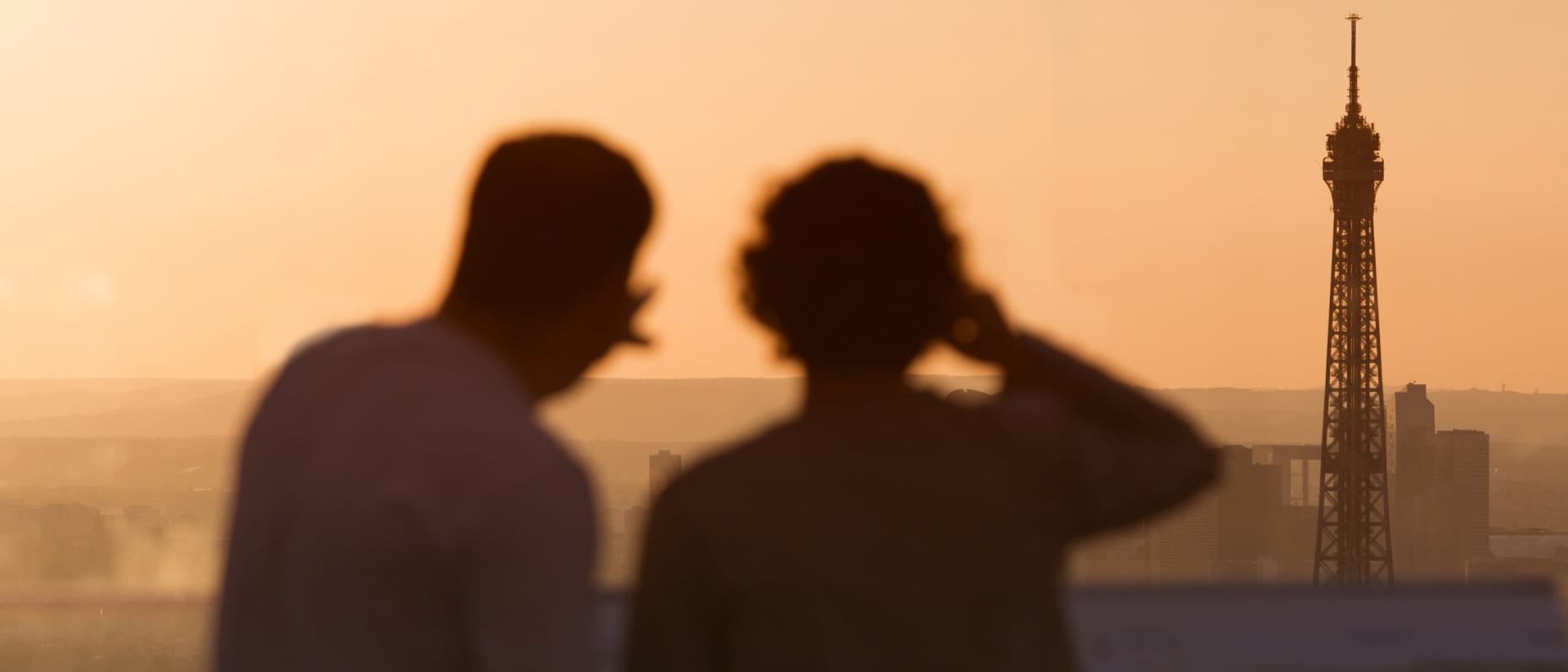 A couple views the Eiffel Tower at dusk from a distance