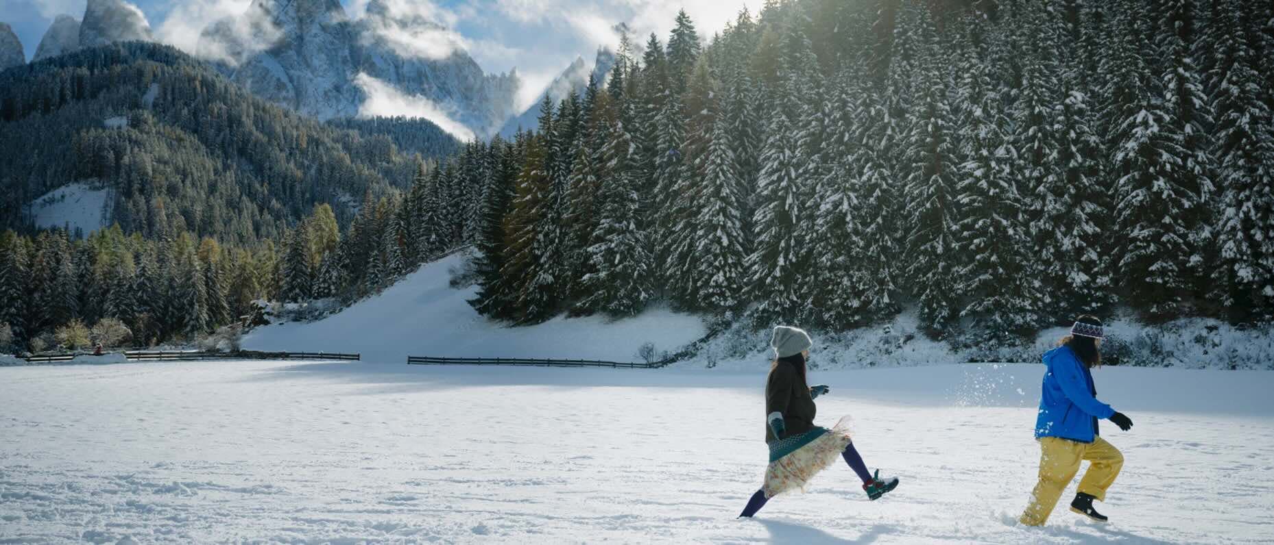 Two people frolick in the snow in a gorgeous mountain setting