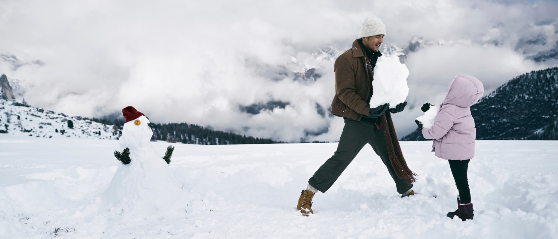 A man and child build a snowman on a misty mountain top