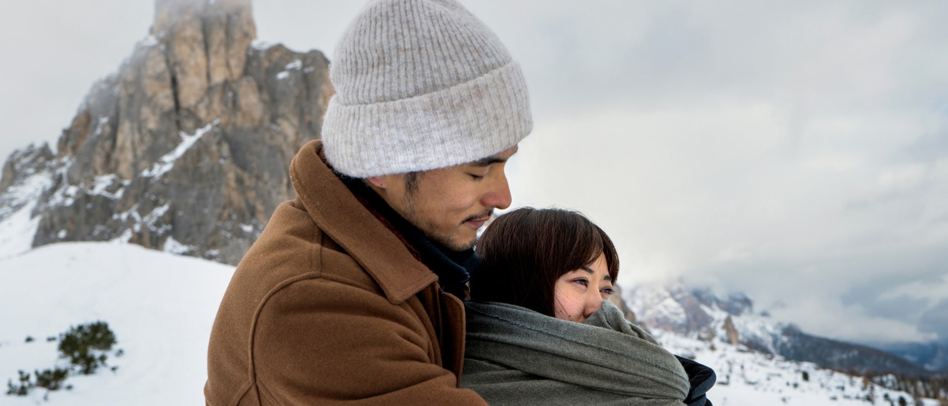 A couple engage in a cosy embrace on a snow covered mountain